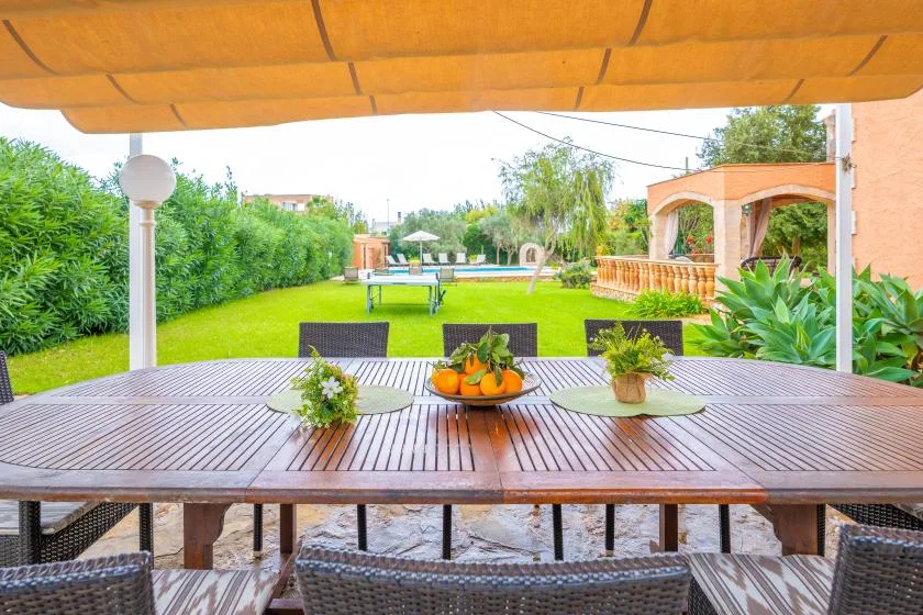 A garden patio with a long outdoor table overlooks a lawn and swimming pool.