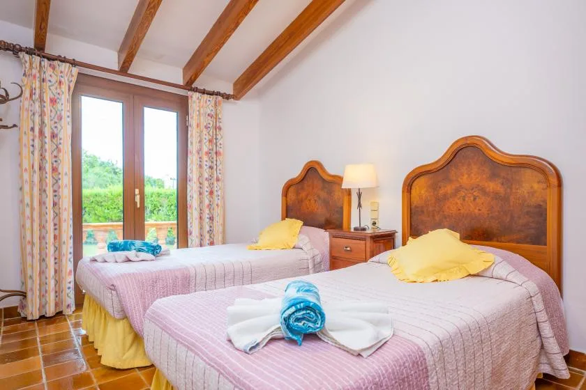 A bedroom with two beds, patterned curtains, and exposed wooden ceiling beams.