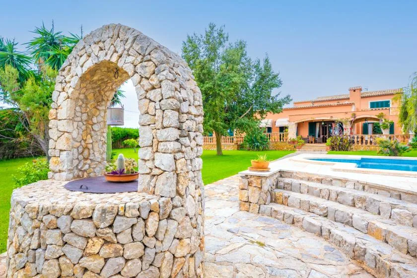 A stone well stands beside a swimming pool and landscaped garden.