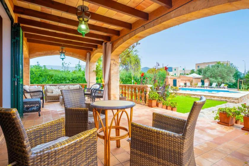 A covered patio with wicker seating overlooks a garden and swimming pool.