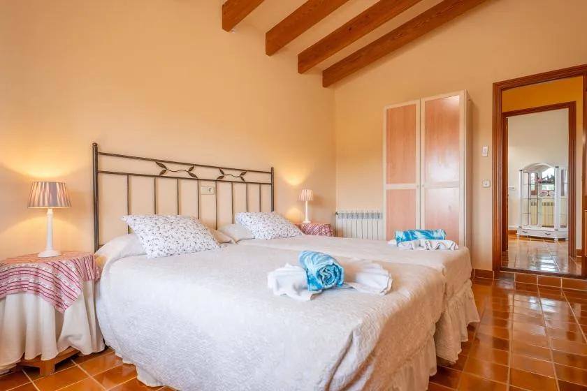 A bedroom with two beds, bedside lamps, and exposed wooden ceiling beams.