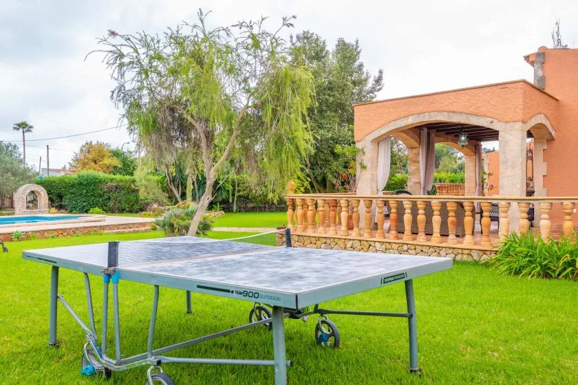 A table tennis table stands on a lawn beside a brick patio.