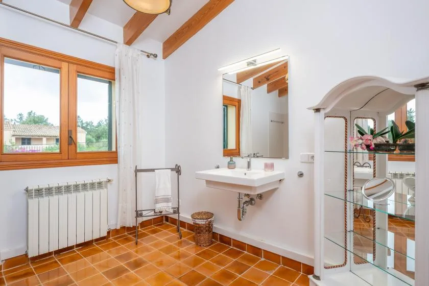 A bright bathroom with a wall-mounted sink, mirror, and wood-framed window.
