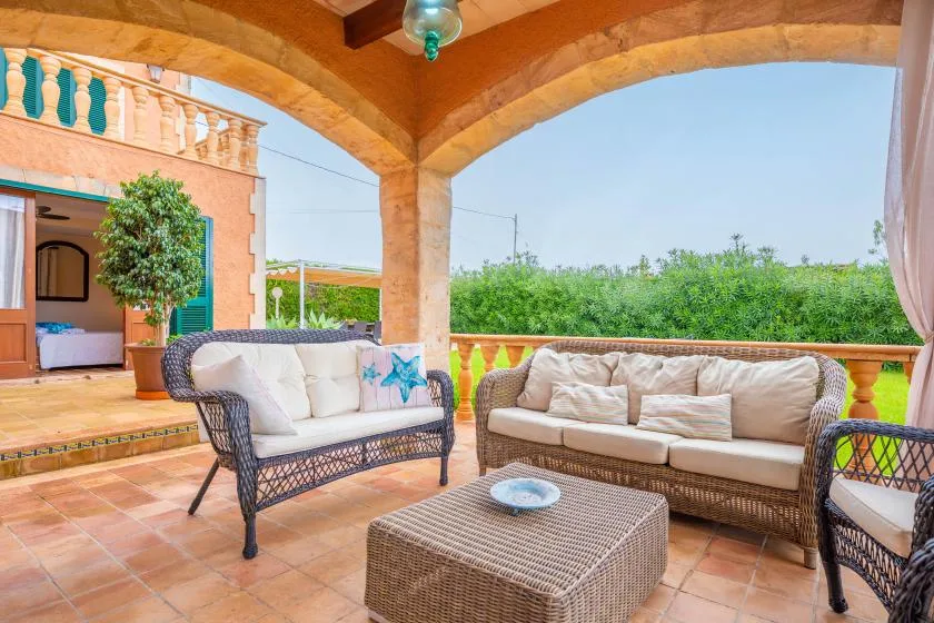 A covered patio seating area with wicker furniture and views of greenery.