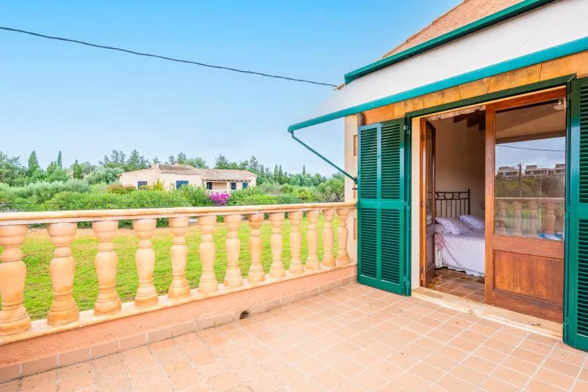 A tiled balcony with a balustrade overlooks greenery, with an open doorway to a bedroom.
