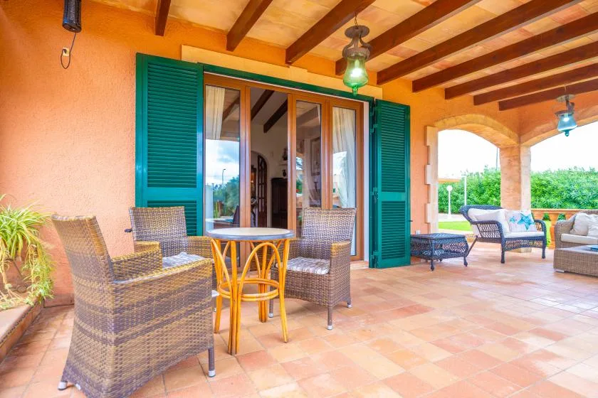 A covered patio with wicker seating, a small table, and open doors.