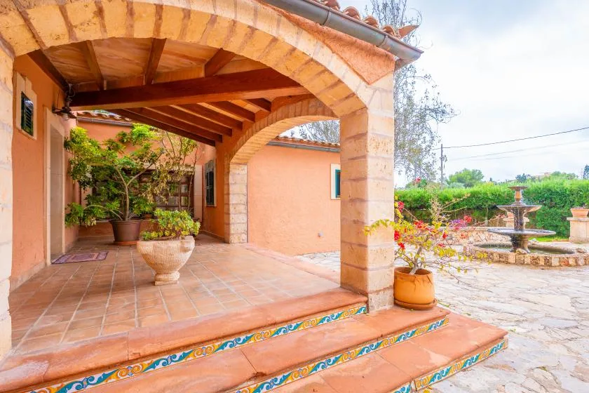 A covered patio with tiled steps, potted plants, and a garden fountain.
