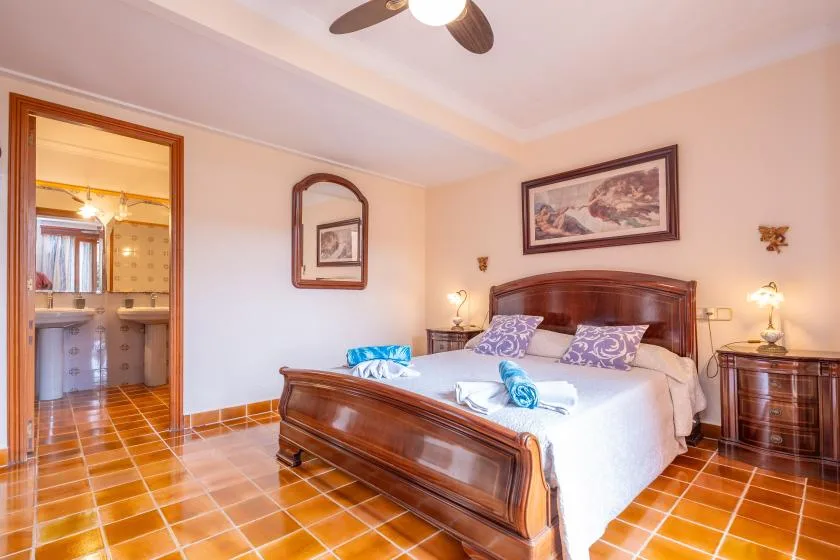 A bedroom with a large bed, wooden headboard, and tiled floor.