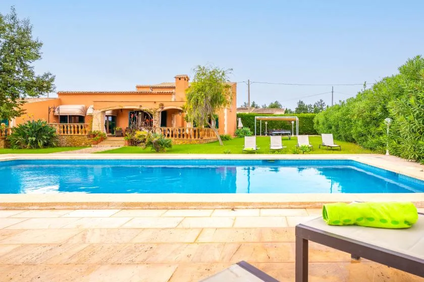 An outdoor swimming pool sits in front of a house and garden.
