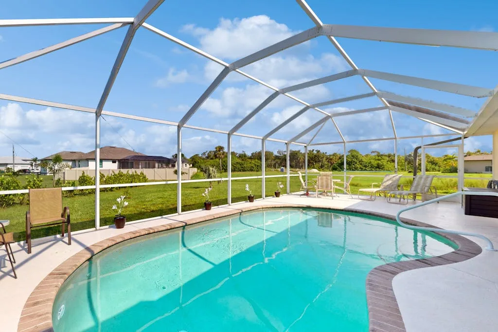 An outdoor swimming pool sits beneath a screened enclosure, with lounge seating nearby.