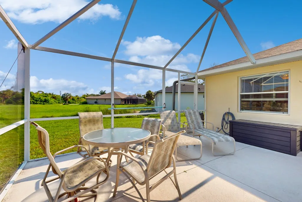 A screened patio with outdoor seating and a round table beside the house.