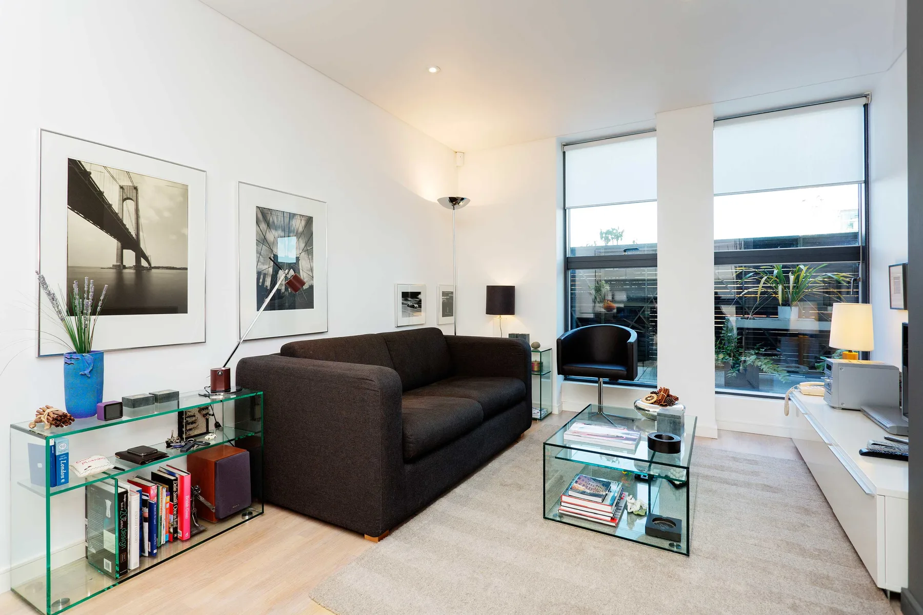 A bright living room with dark seating, framed wall art, and large windows.