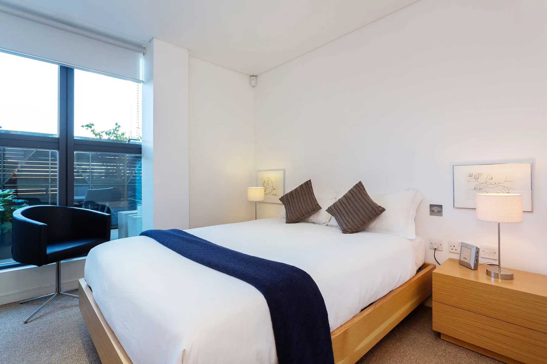 A bright bedroom with a white bed and large windows.