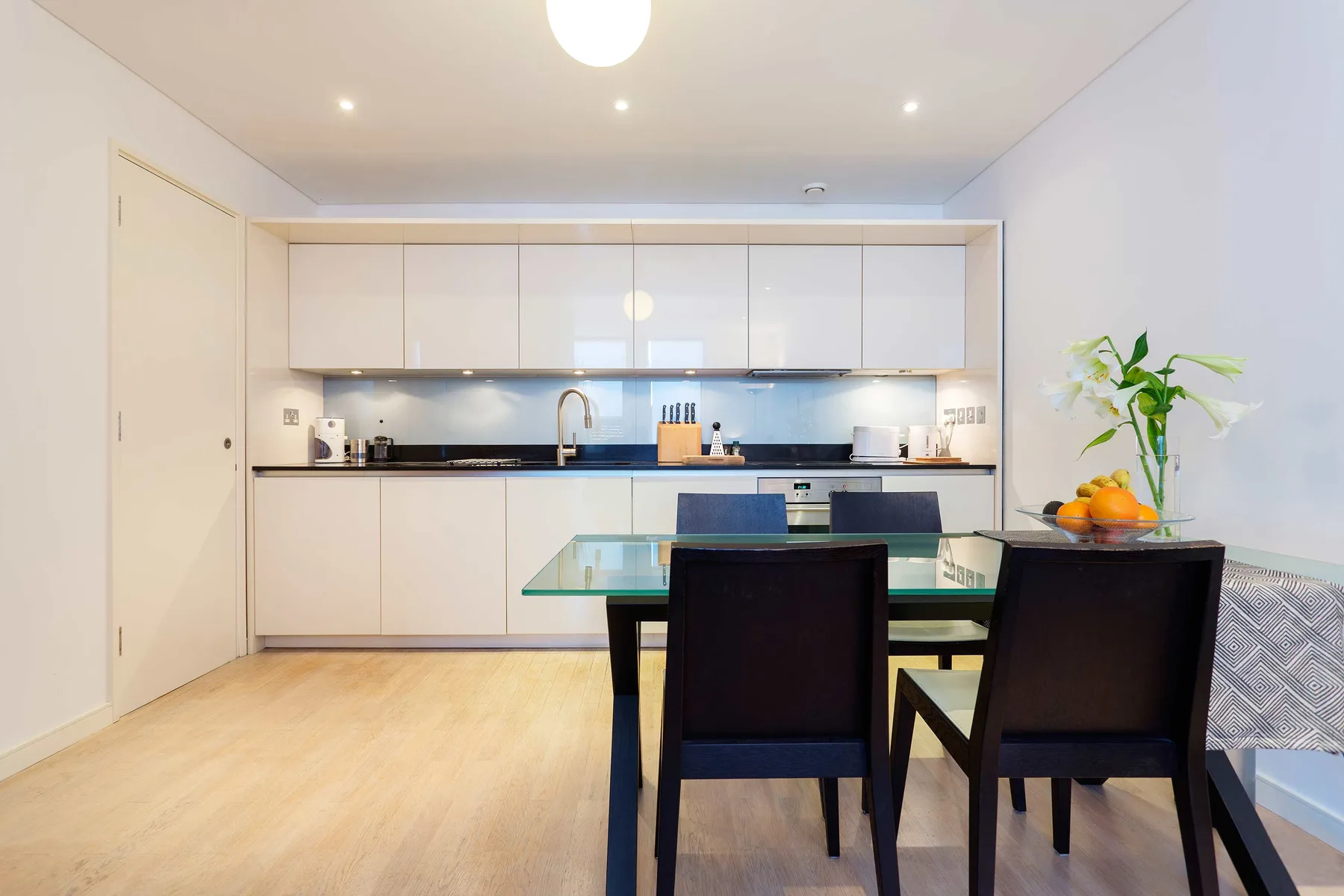 A dining area with a glass table and a kitchen in the background.