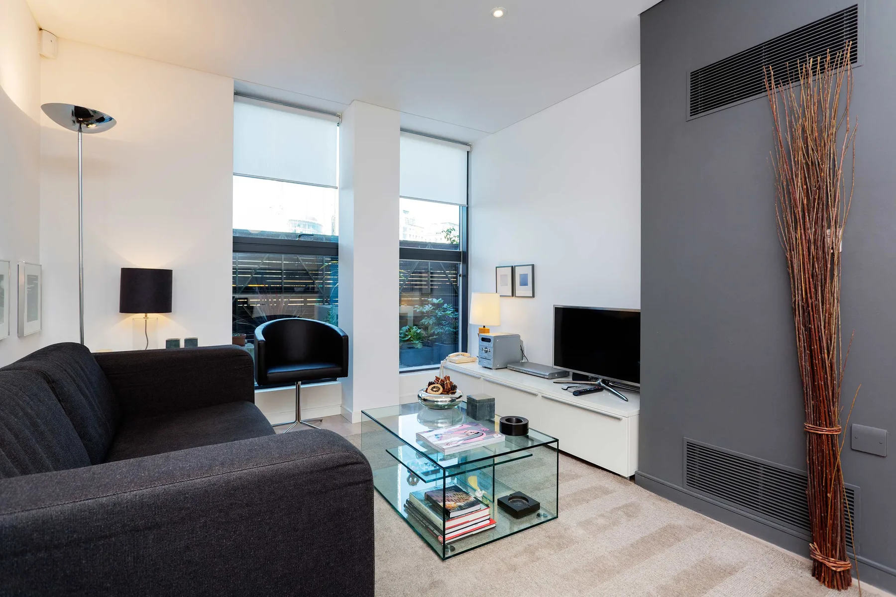 A modern living room with dark seating, a glass coffee table, and a television.