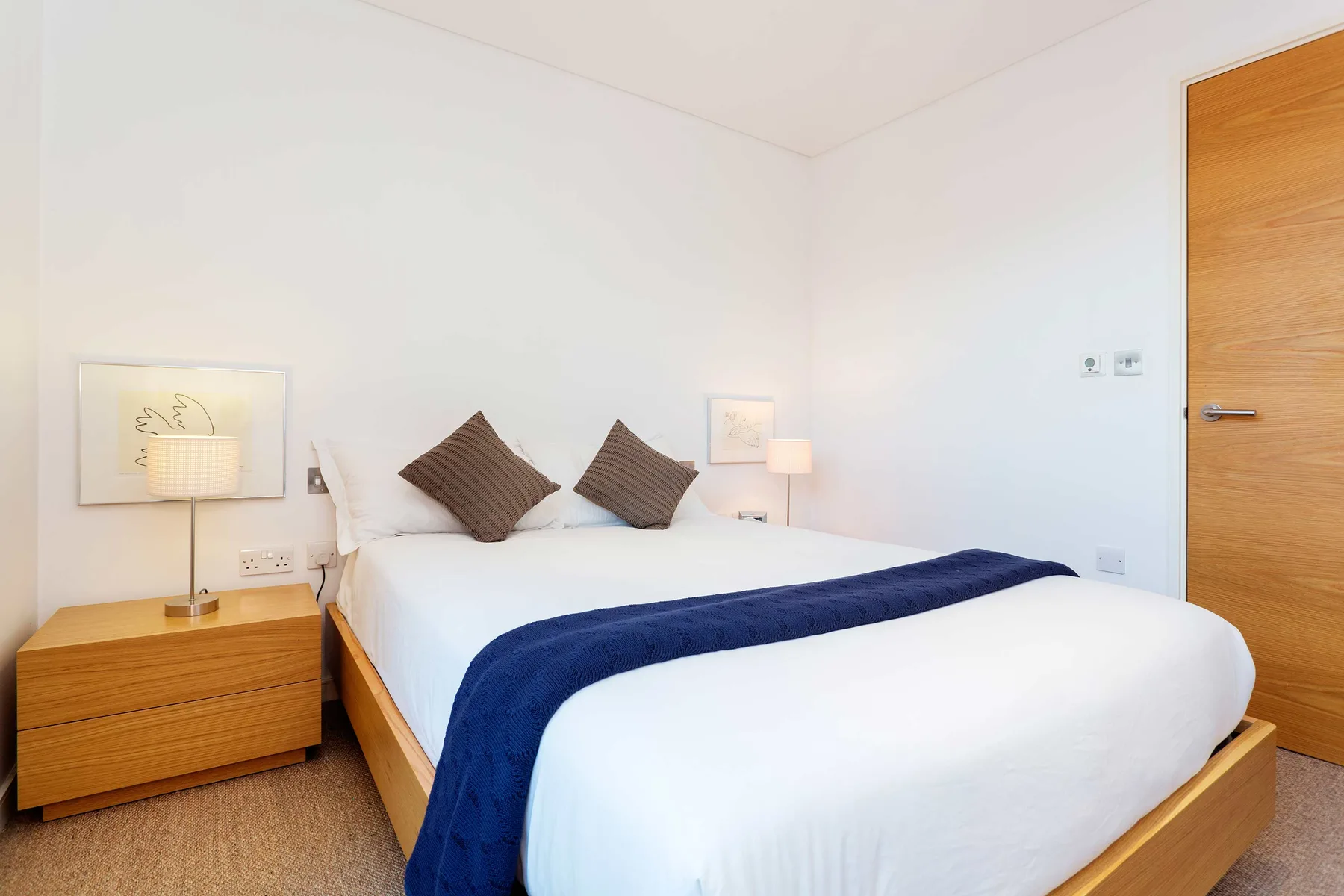 A bright bedroom with a neatly made bed and a wooden bedside table.
