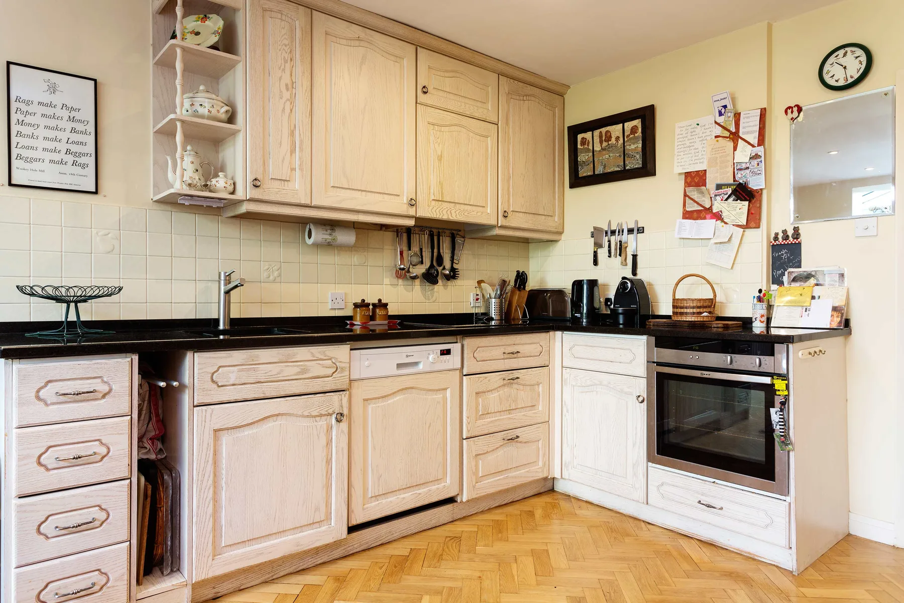 A fitted kitchen with light wood cabinets, dark countertops, and a herringbone floor.