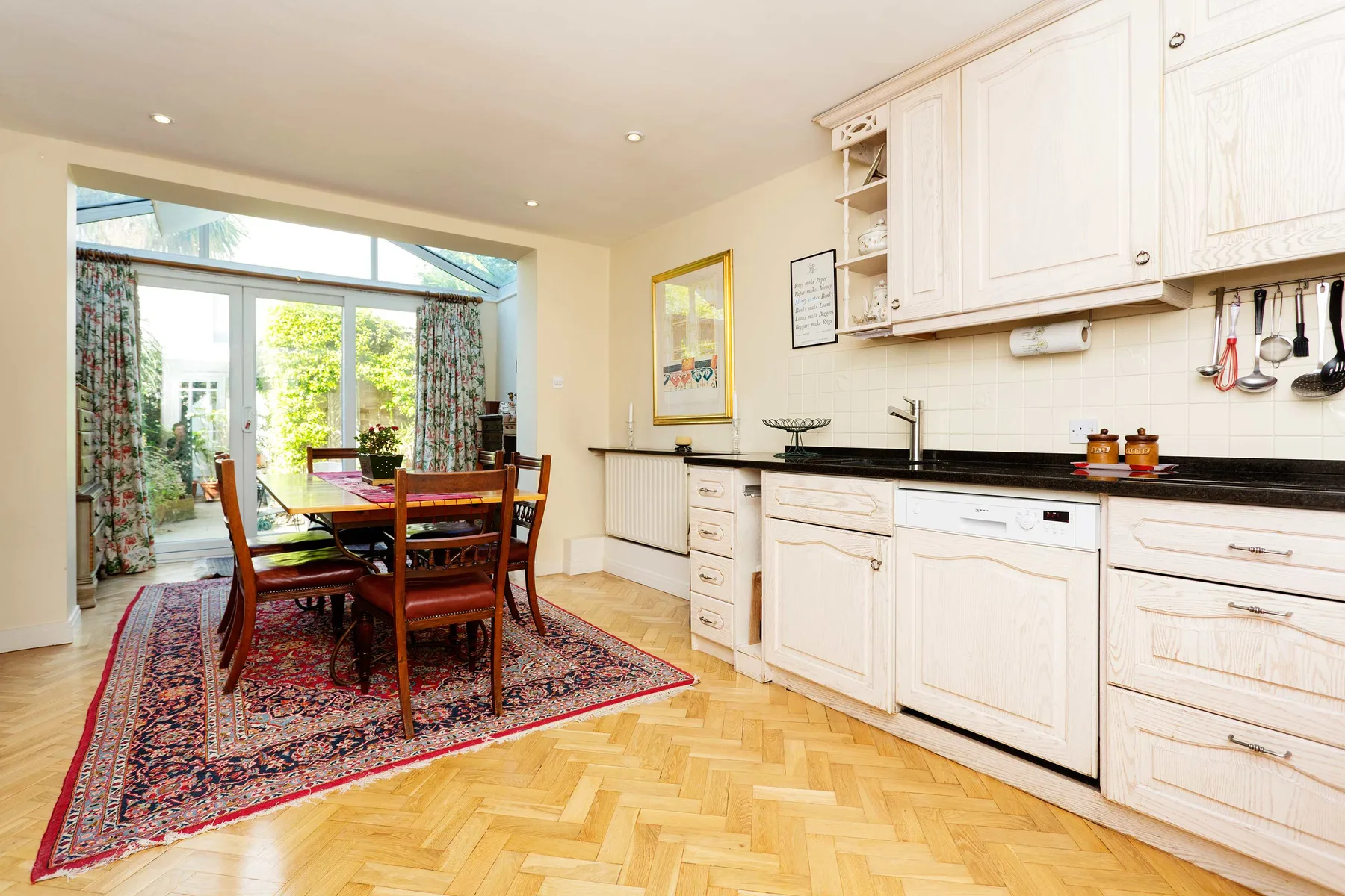 A bright kitchen and dining area with a wooden table beside large windows.
