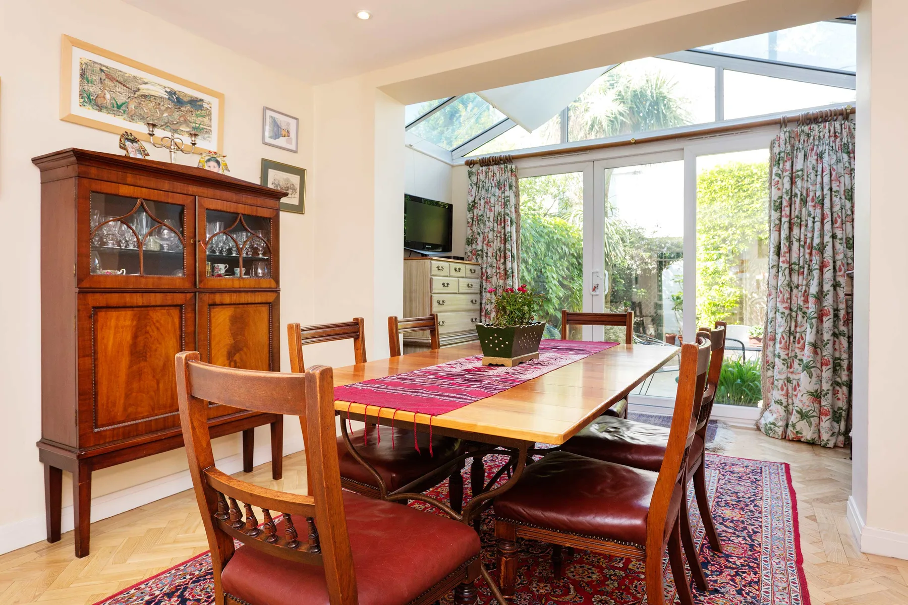 A dining room with a long wooden table and large windows overlooking greenery.