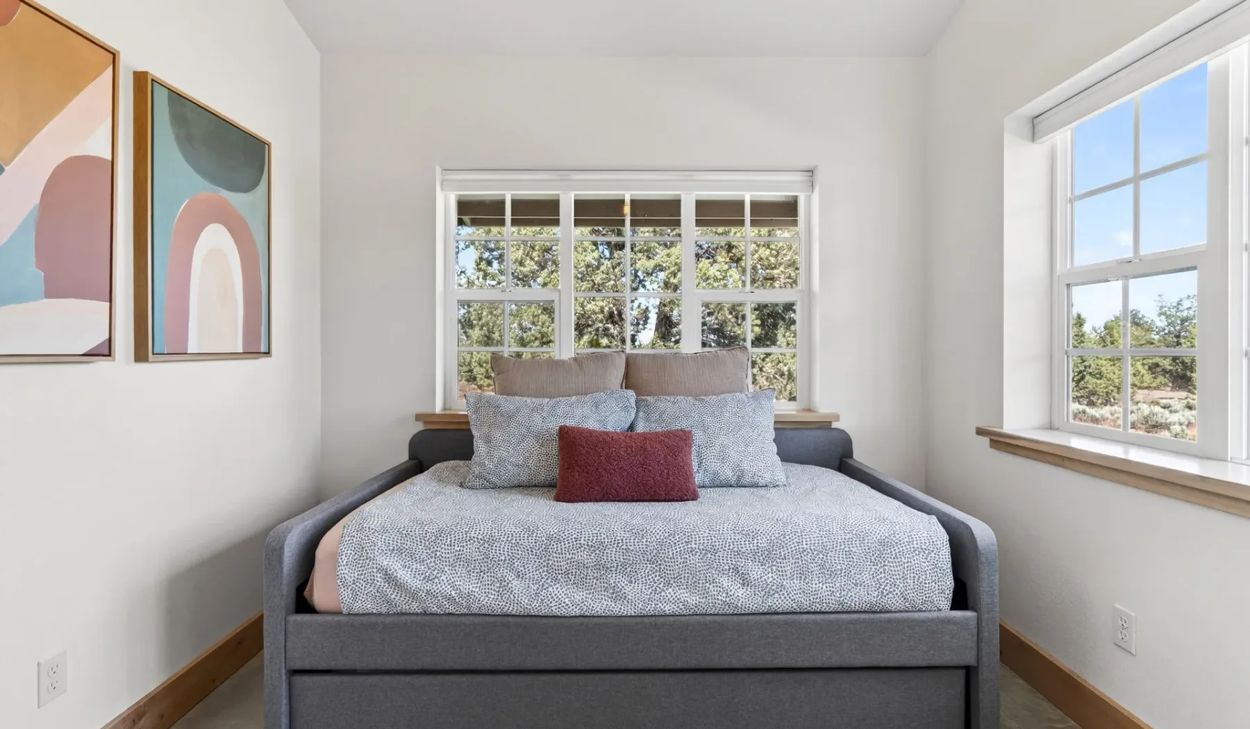 Una cama bien arreglada está entre dos ventanas en un dormitorio luminoso.