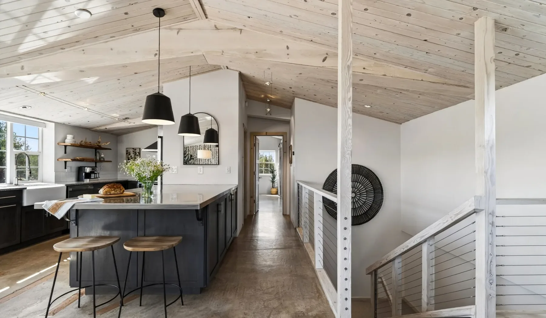 Una cocina abierta y zona de comedor junto a una escalera, bajo un techo inclinado de madera.