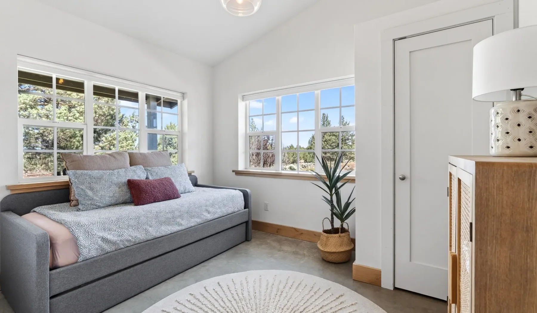 Un dormitorio luminoso con una cama gris y ventanas grandes.