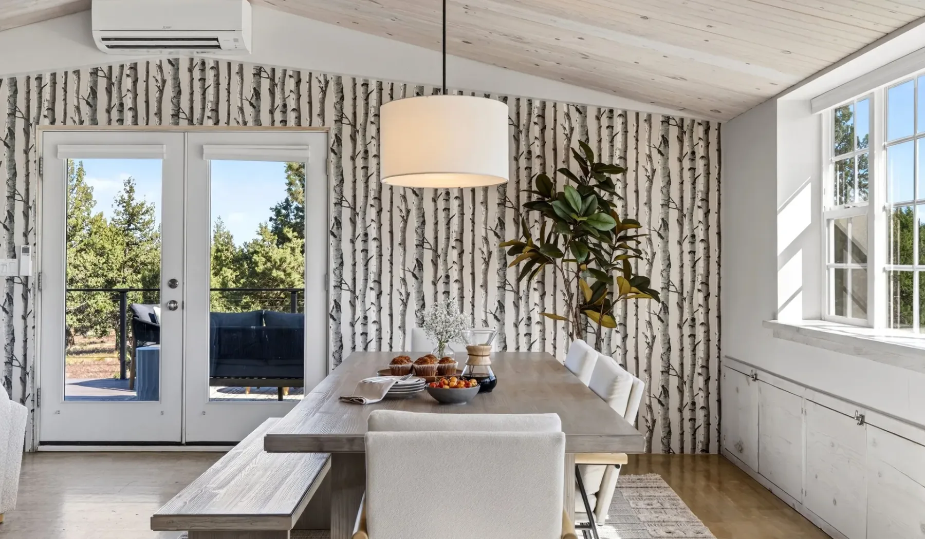 Un comedor luminoso con una mesa larga, una lámpara colgante y ventanales.
