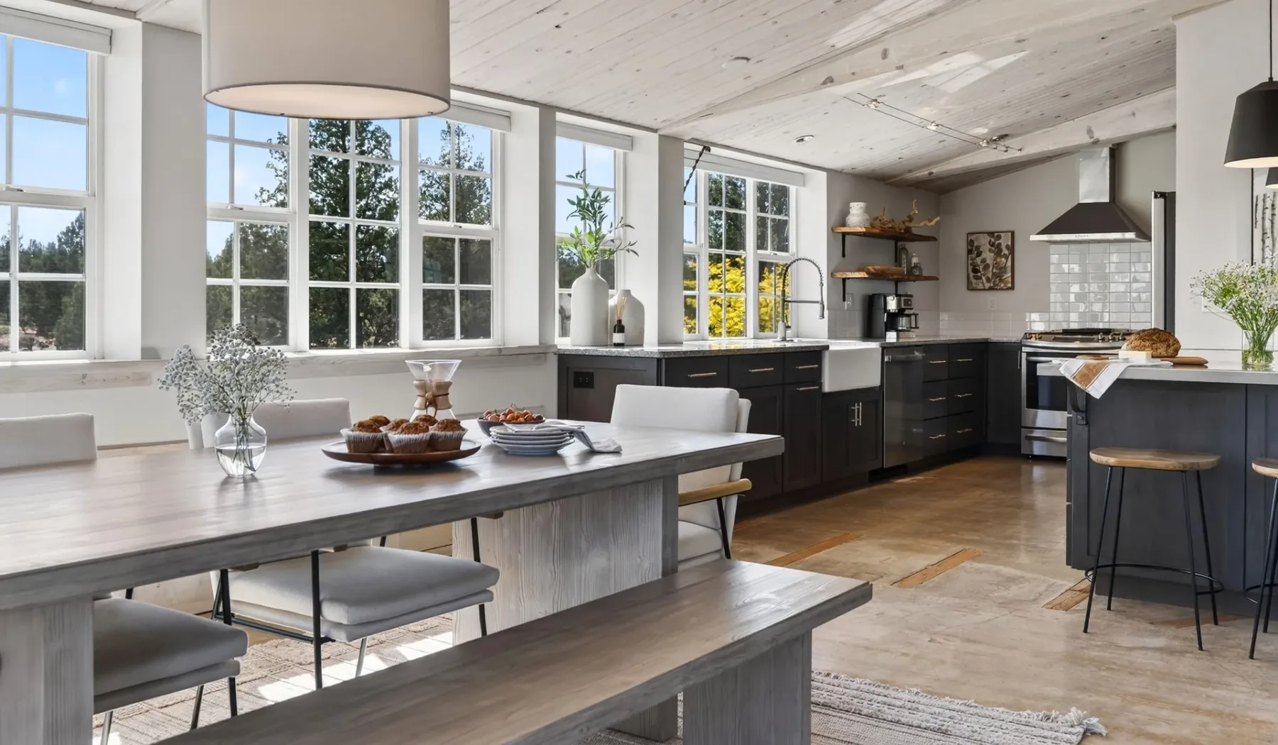 Cocina y comedor luminosos con gabinetes oscuros y una mesa larga.