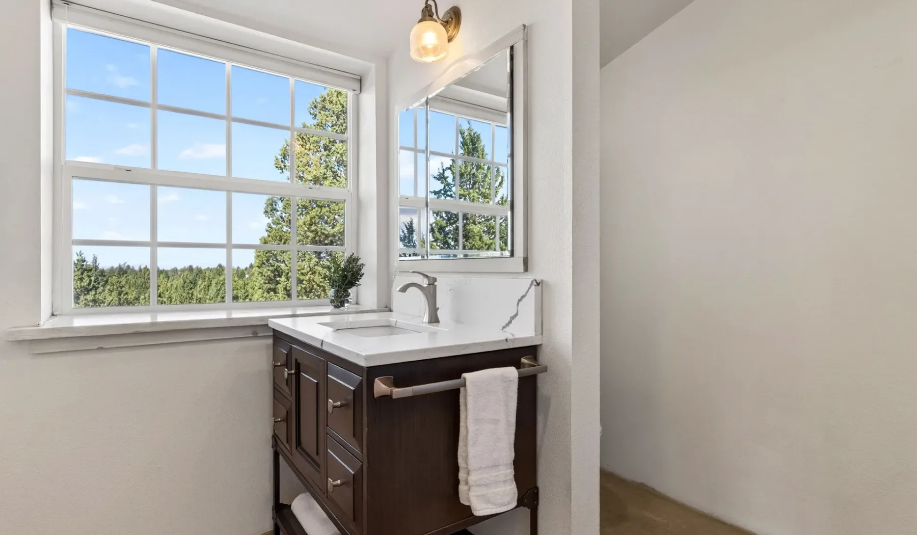Un tocador de baño está junto a una ventana grande con vistas a la vegetación.