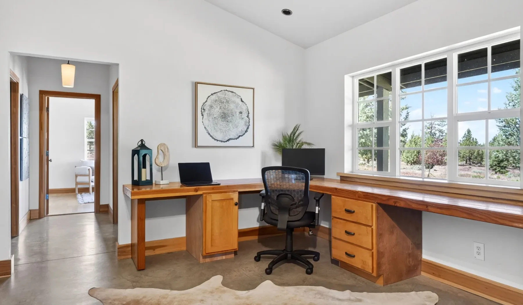 Un despacho luminoso con escritorio de madera, silla y ventanas grandes.