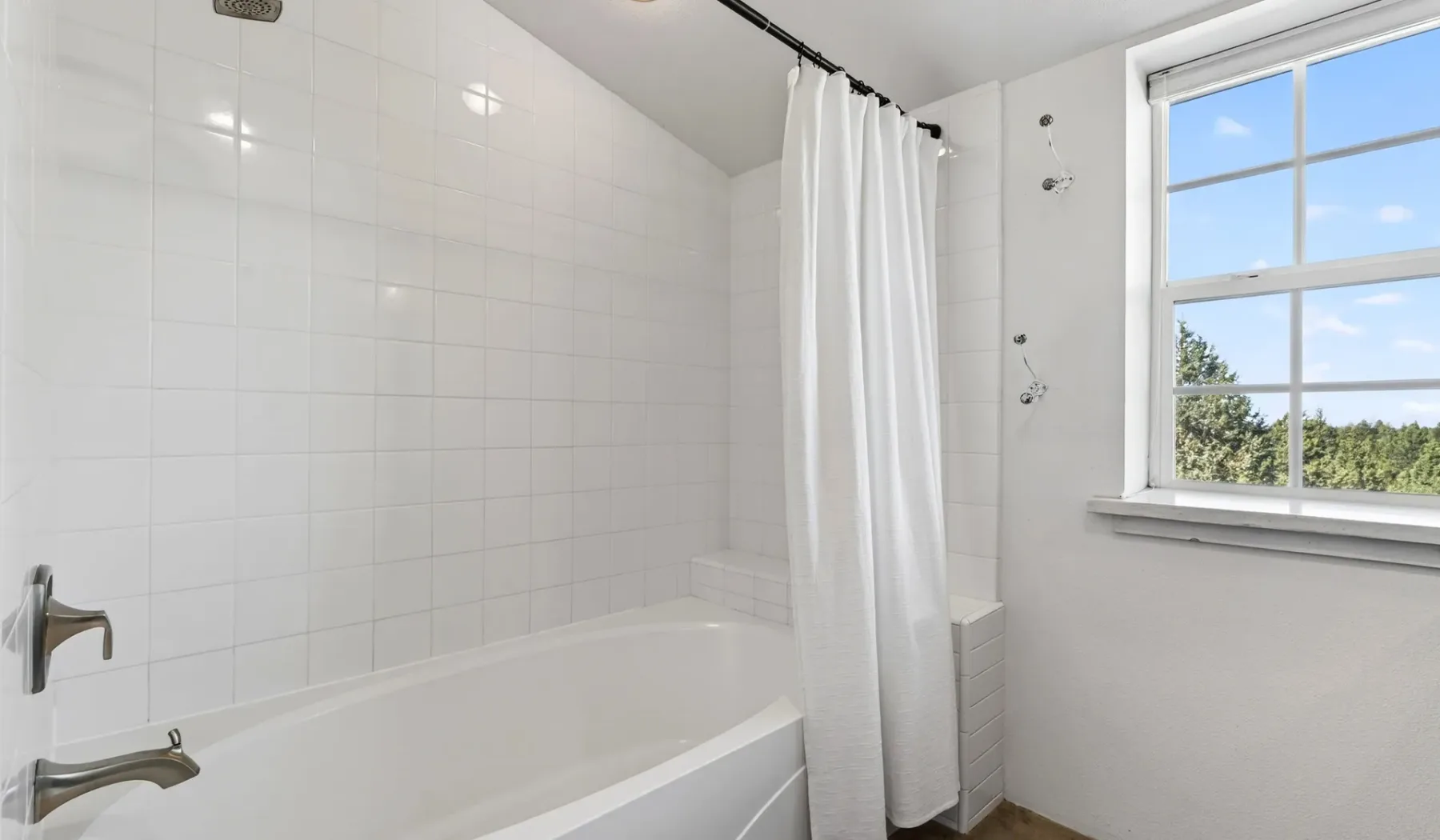 Un baño alicatado con bañera, cortina de ducha y ventana.