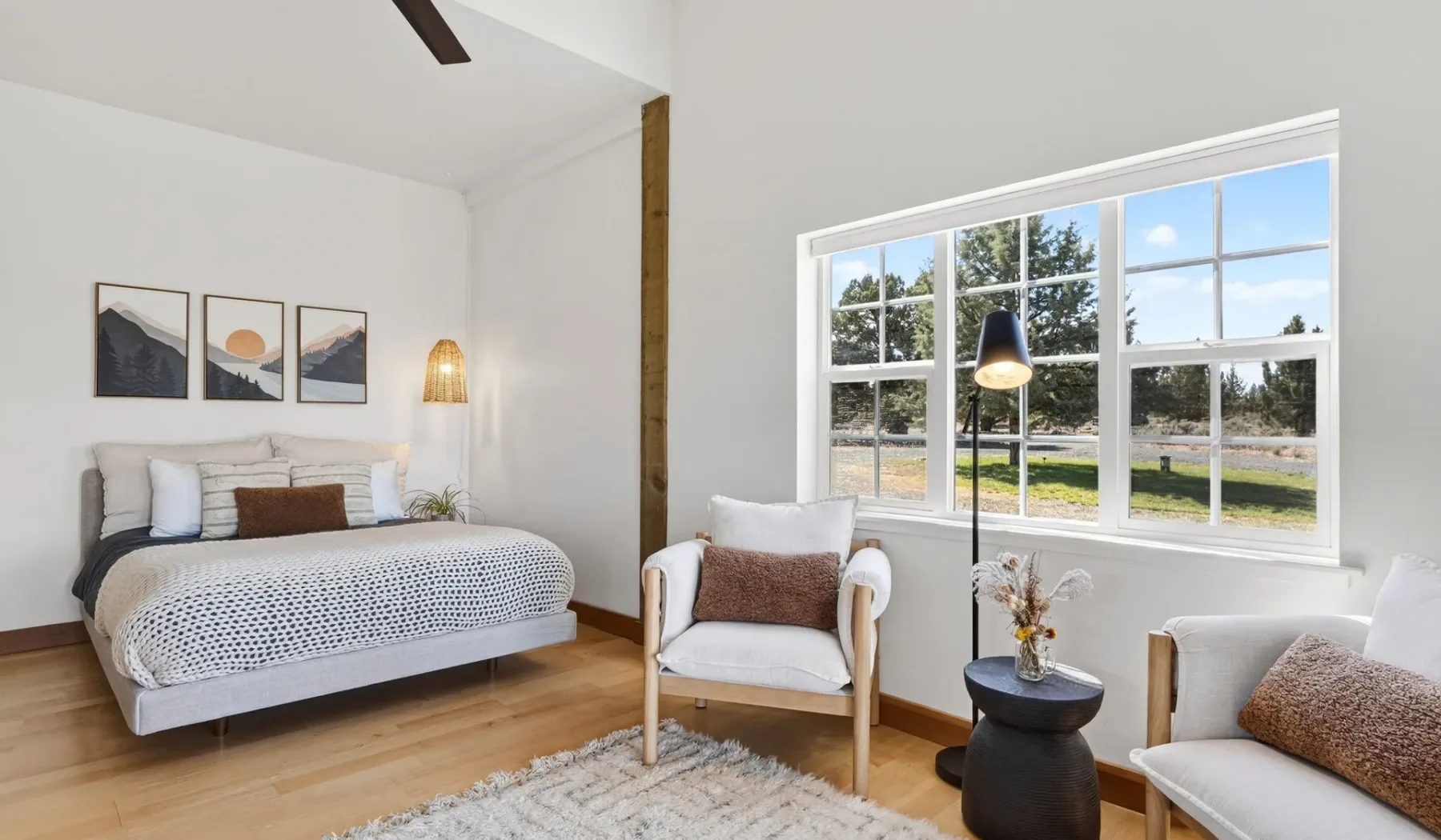 Un dormitorio luminoso con una cama, un sillón y ventanas grandes.