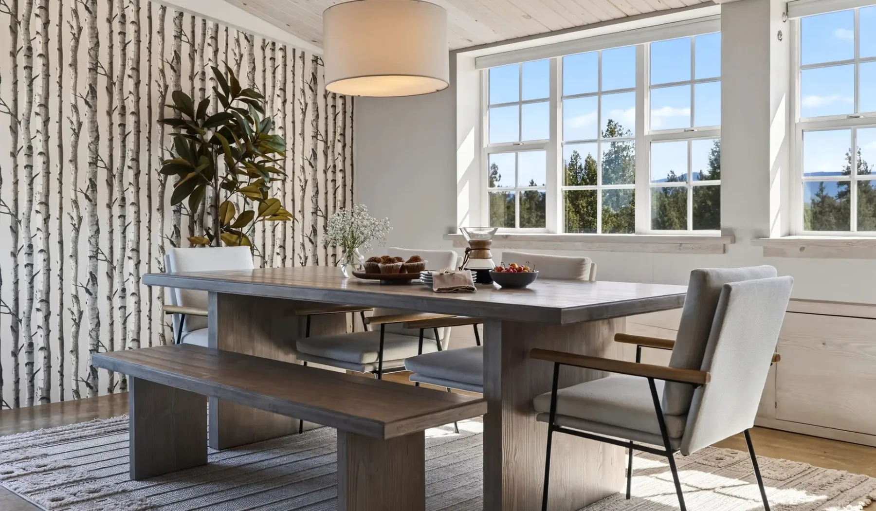 Un comedor luminoso cuenta con una mesa larga y grandes ventanas.