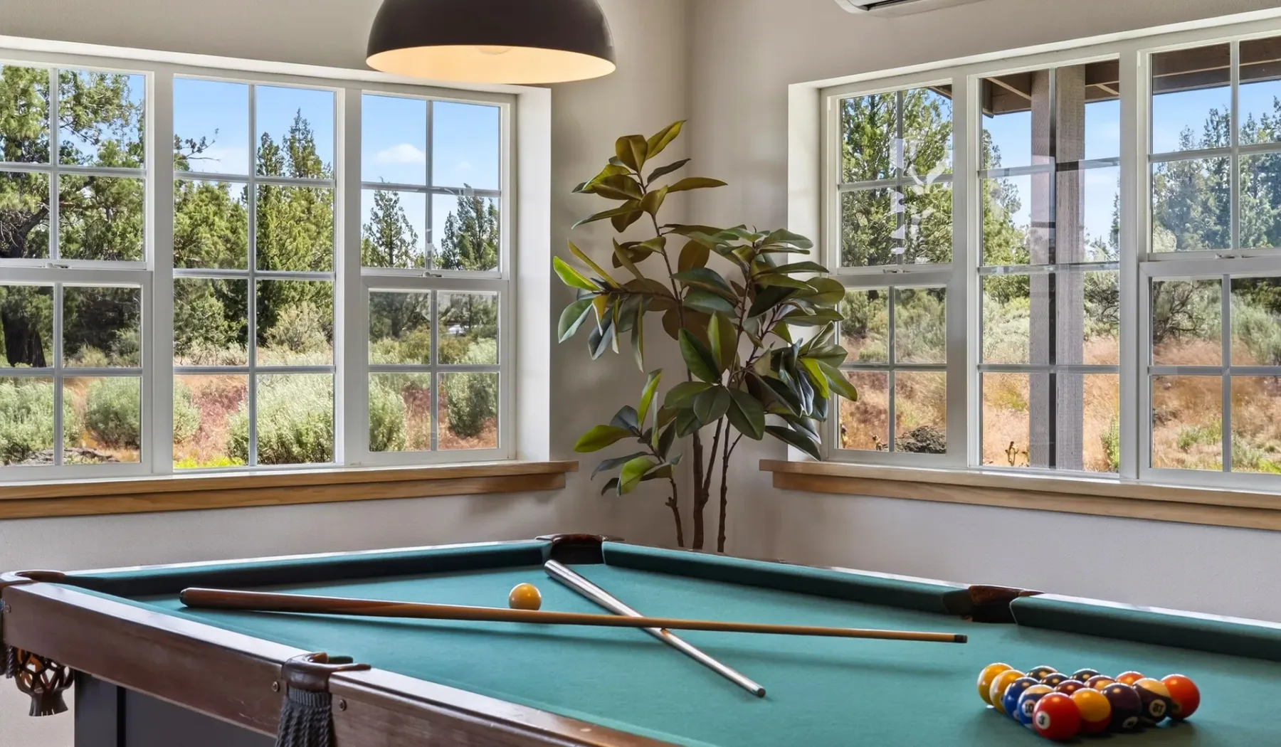 Una sala de billar con una mesa junto a grandes ventanas.