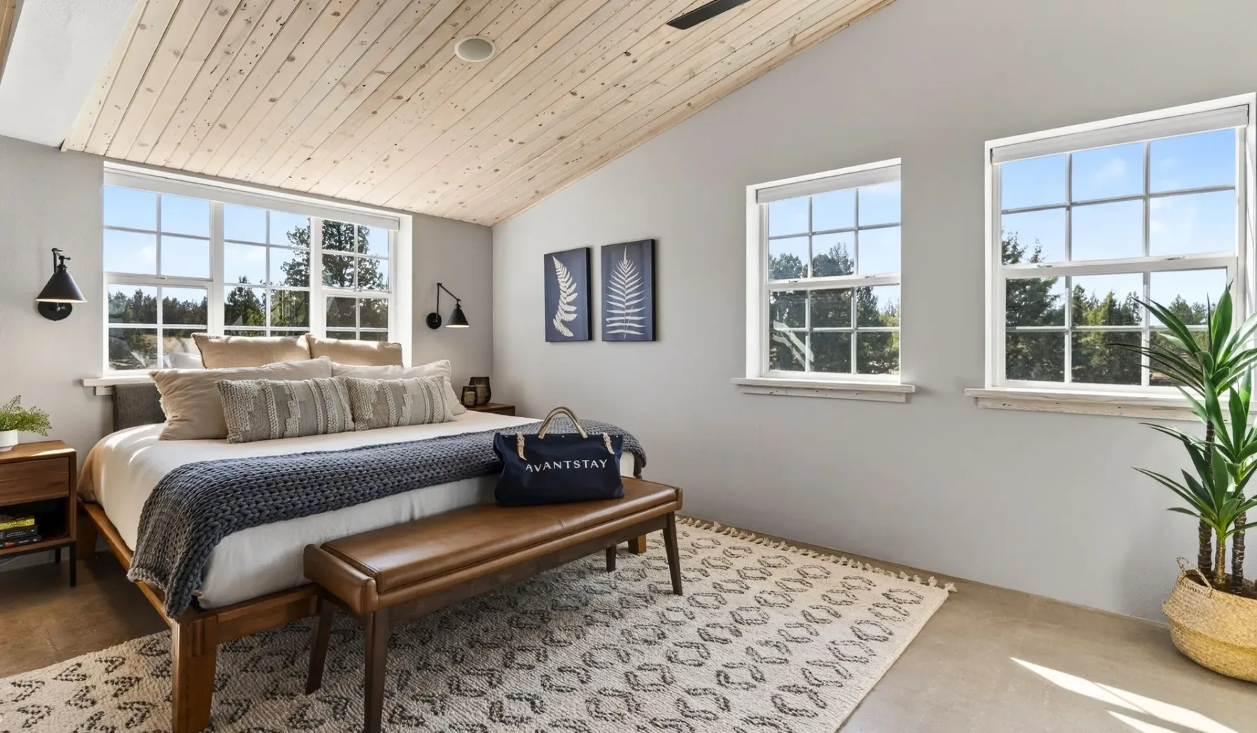 Un dormitorio luminoso con una cama, un banco y ventanas amplias.