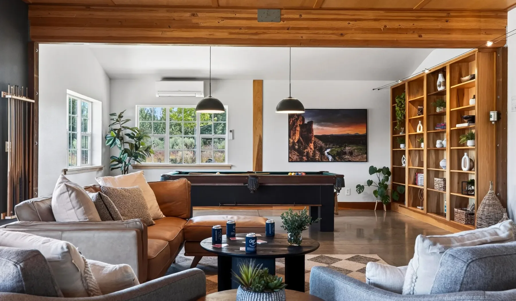 Una sala de estar con sofás, una mesa de billar y una estantería alta de madera.