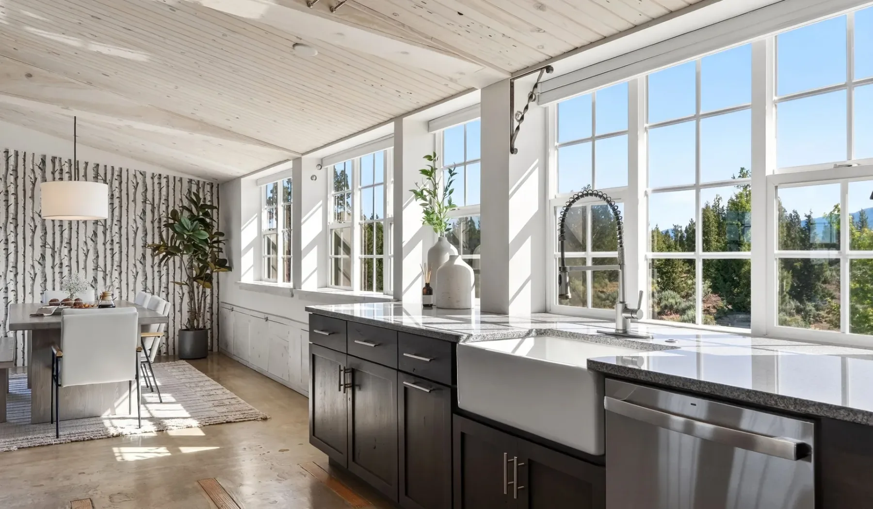 Una cocina luminosa con gabinetes oscuros y grandes ventanas con vistas a la vegetación.