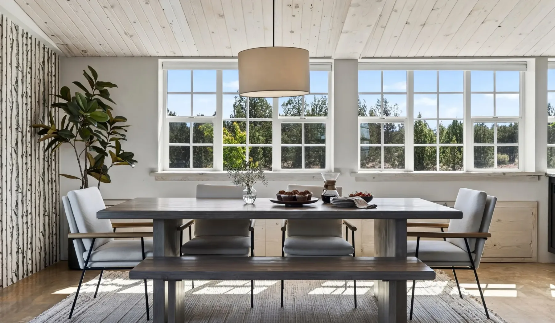 Un comedor luminoso con una mesa larga y grandes ventanas.
