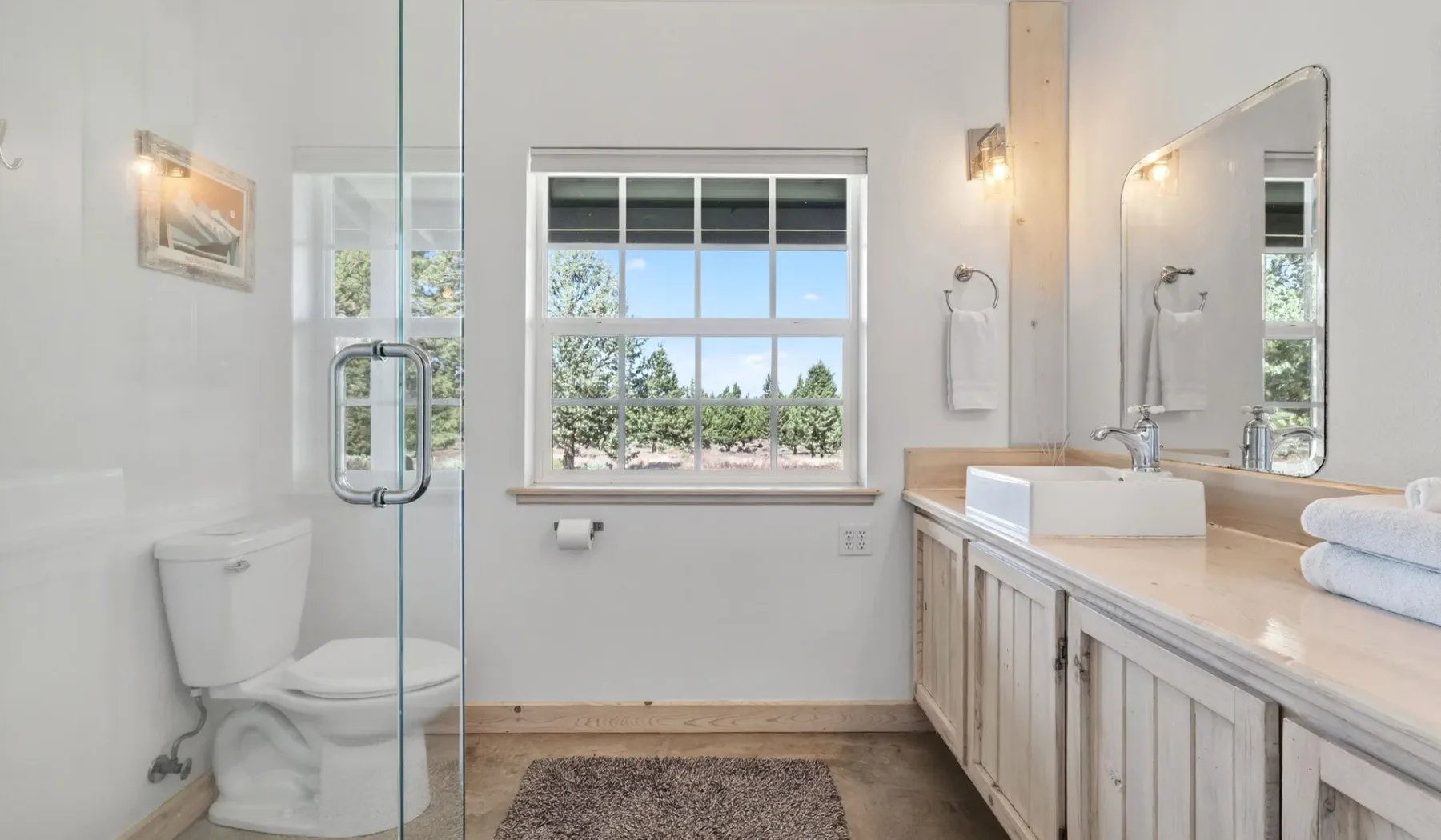 Un baño luminoso con ventana, tocador y ducha de vidrio.