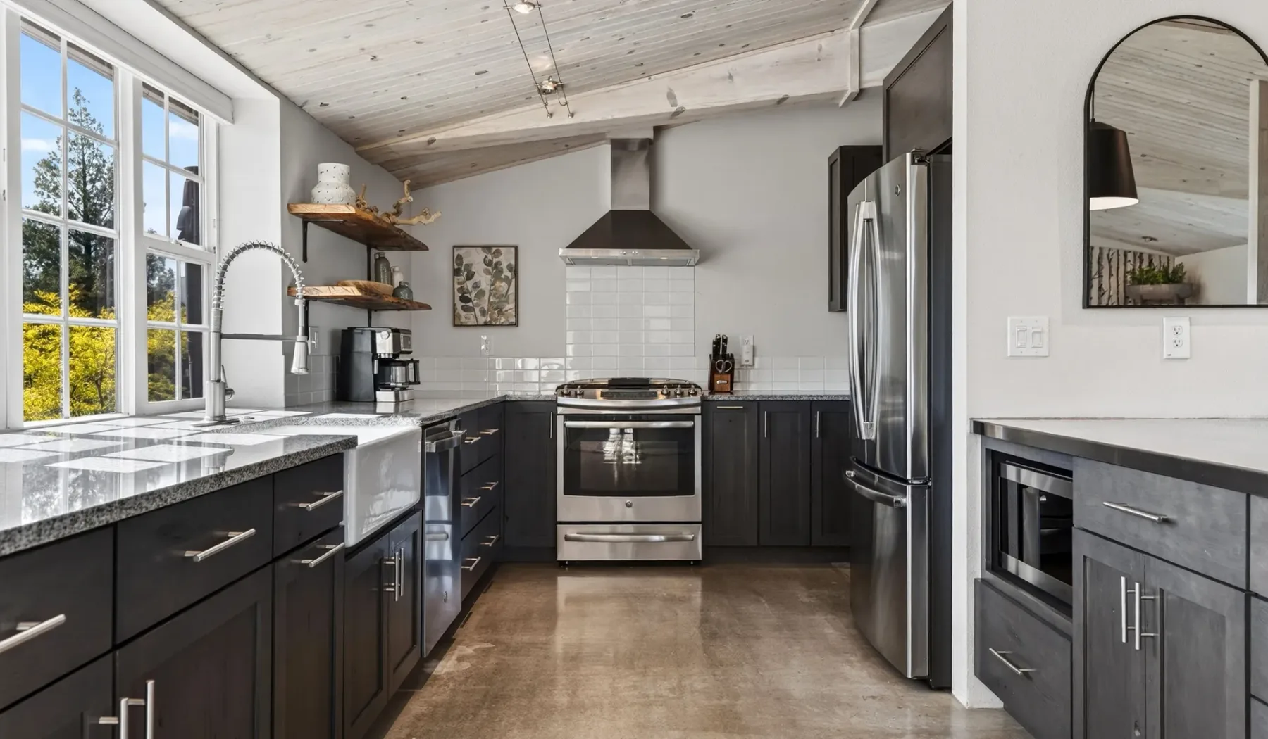Una cocina con gabinetes oscuros, una estufa central y ventanas grandes.