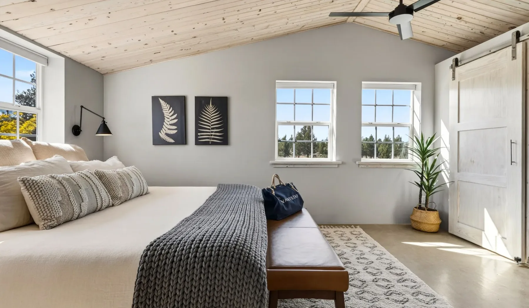 Un dormitorio luminoso con una cama, dos ventanas y una planta en maceta.