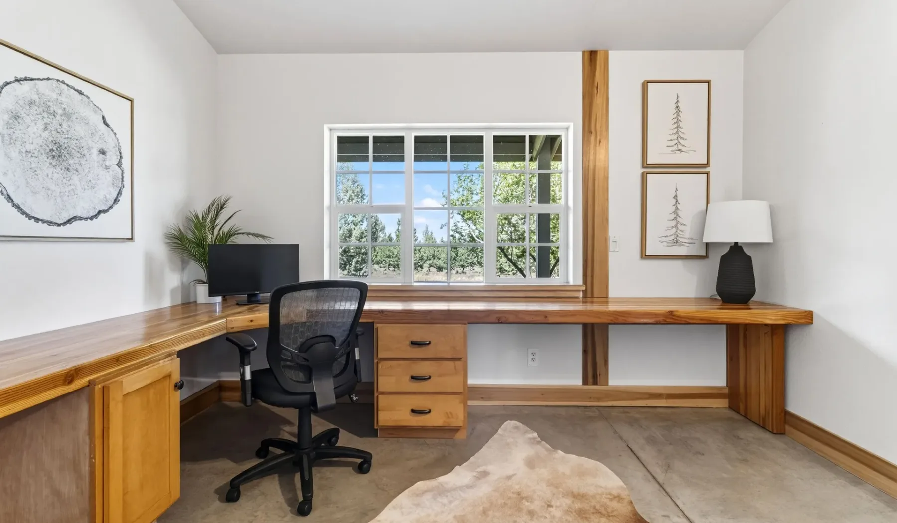 Un despacho en casa con un escritorio largo de madera y una ventana con vistas a la vegetación.