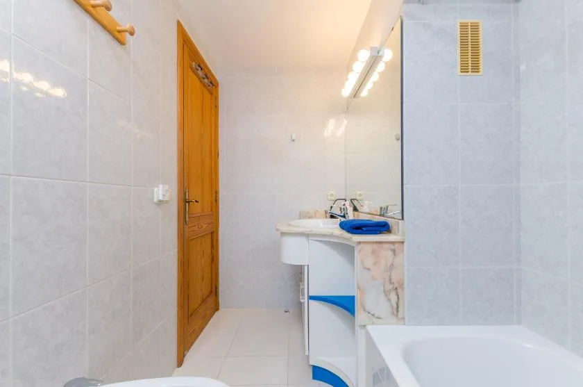 A tiled bathroom with a wooden door, sink, and bathtub.