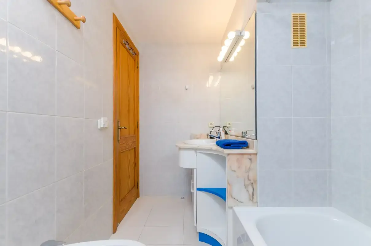 A tiled bathroom with a sink, mirror, and wooden door.