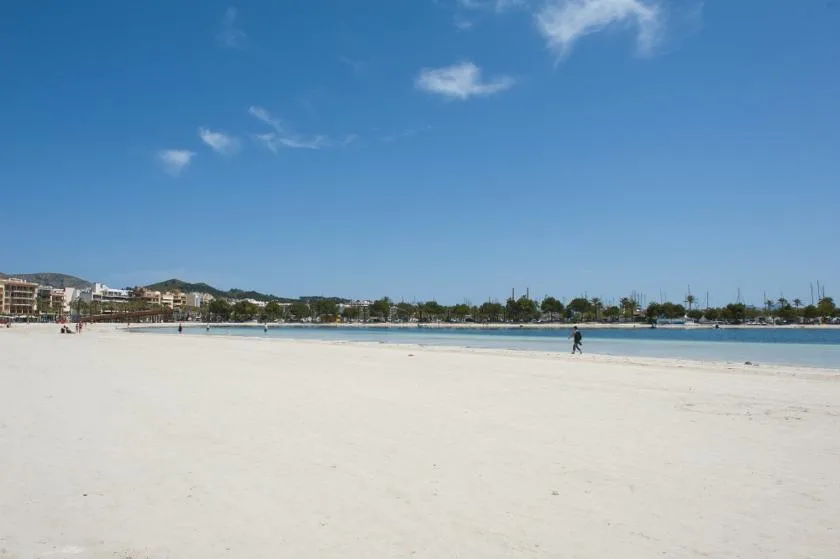 A broad sandy beach stretches toward calm blue water under a clear sky.