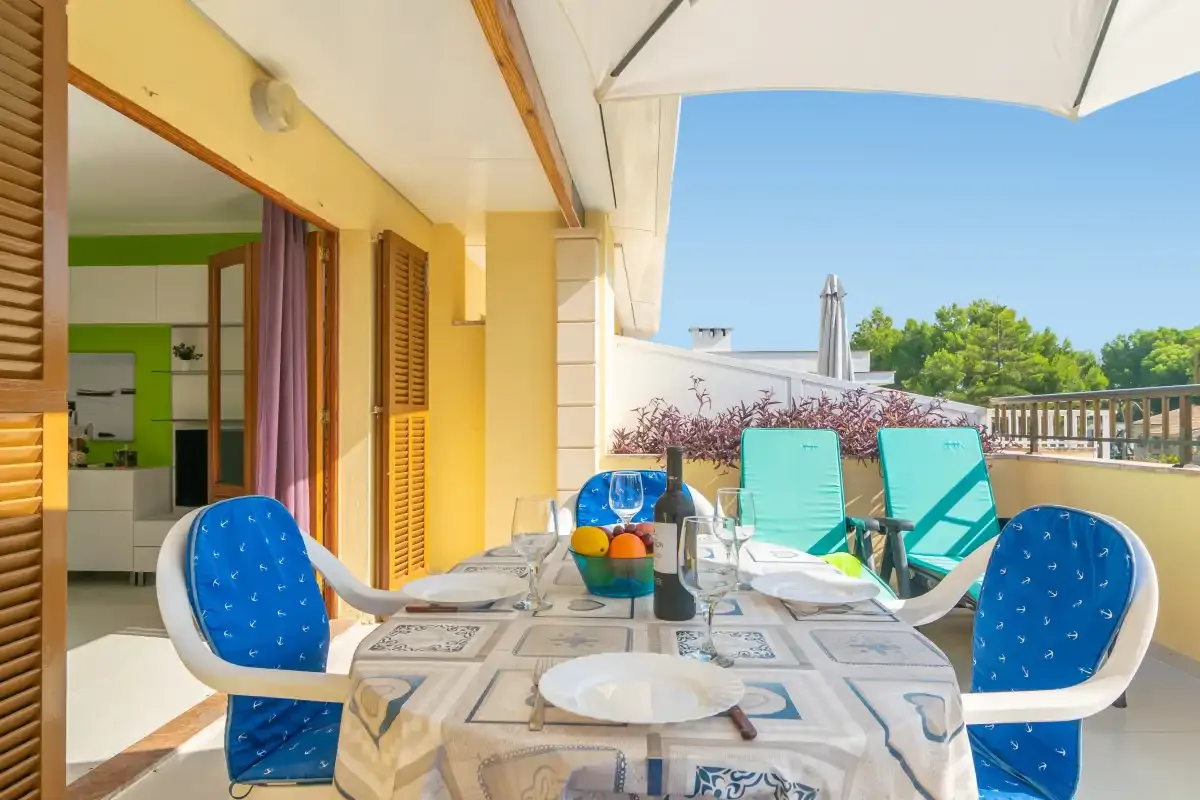 Outdoor dining area with a table and blue chairs beside a sunny terrace.