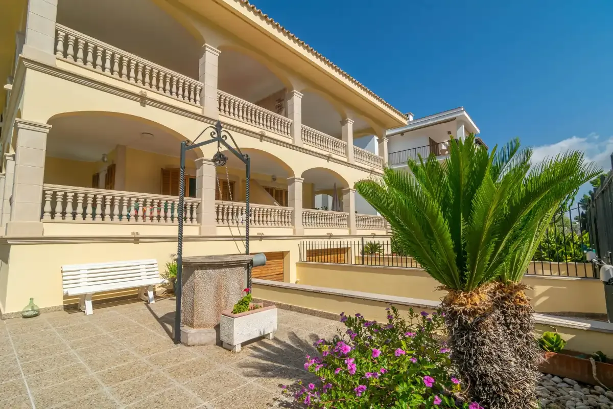 A sunny villa terrace with covered balconies and flowering plants.