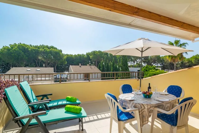 Una terraza soleada tiene una mesa de comedor, asientos y vistas abiertas a los árboles.