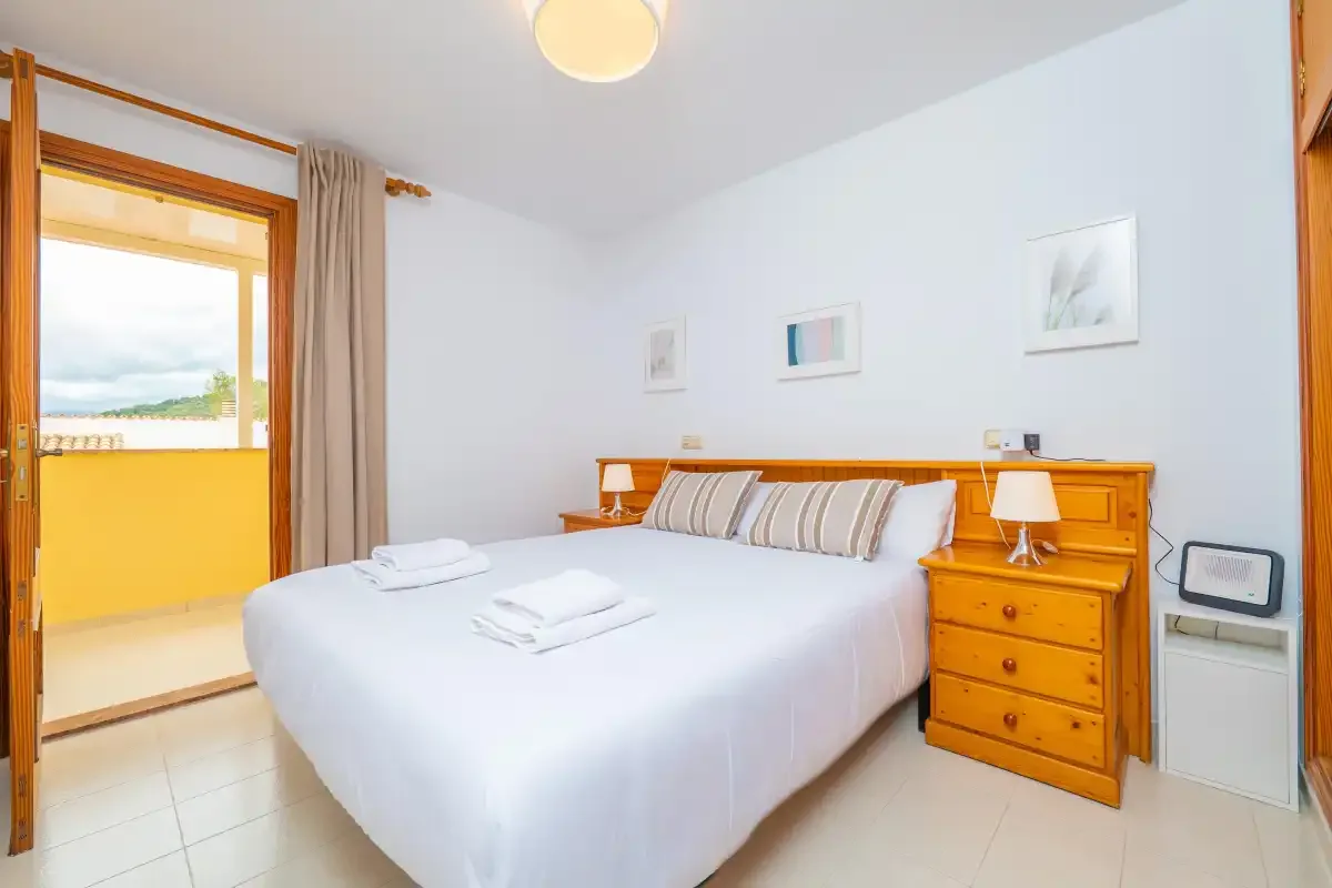 A bright bedroom with a neatly made bed and a wooden dresser.