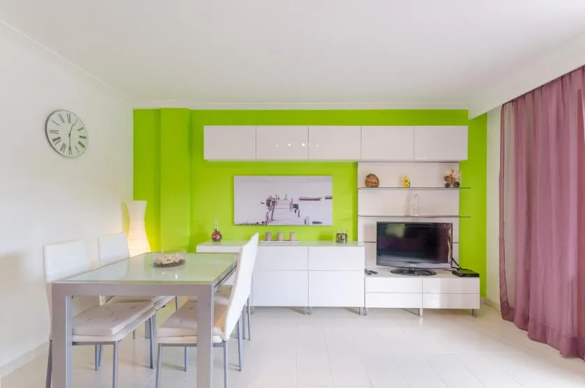 A bright living room with a dining table and a television against a green wall.